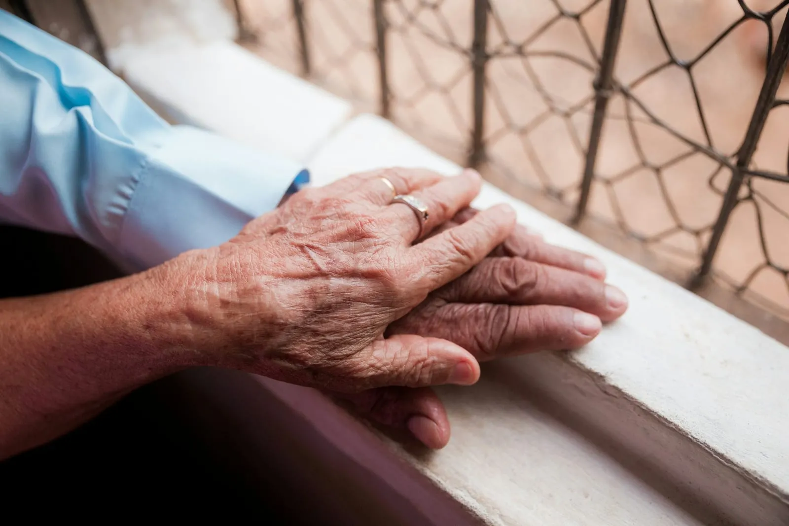 Eine ältere Hand liegt auf einer anderen Hand, auf einem hellen Fensterbrett