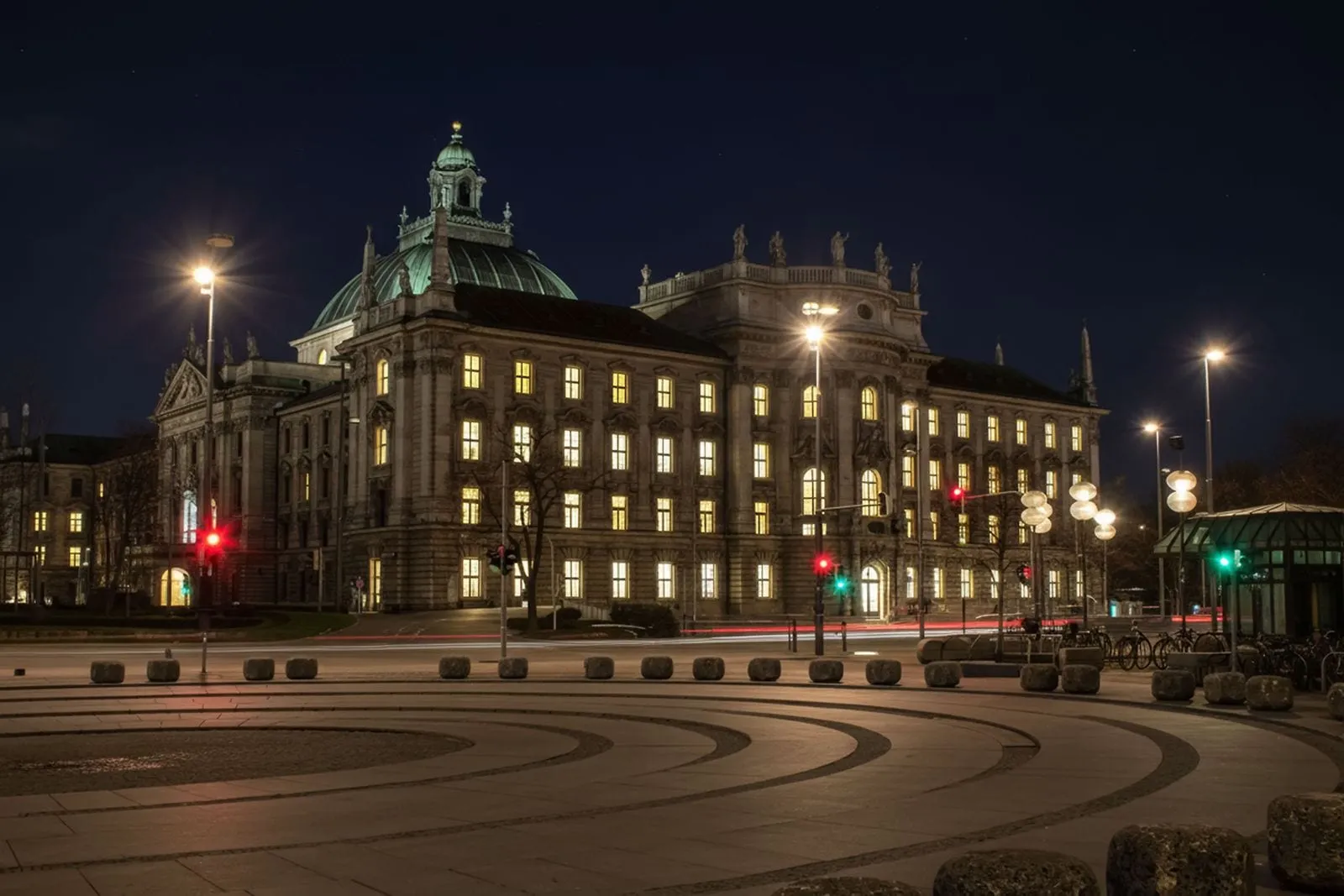 Der beleuchtete Justizpalast in München bei Nacht, davor Straßenbahngleise