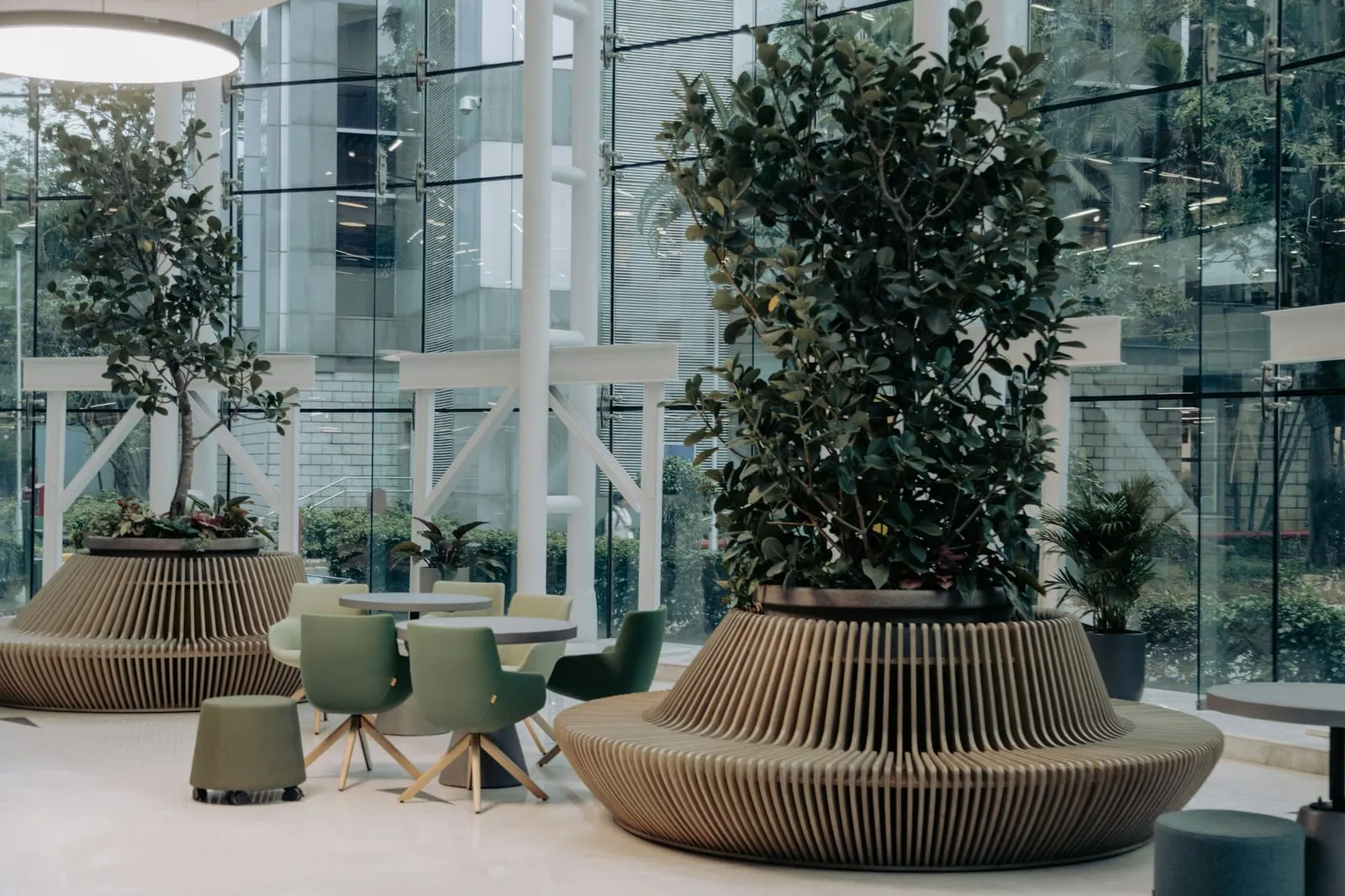 Helles Atrium mit großen Pflanzkübeln, grünen Stühlen und Glasfassade